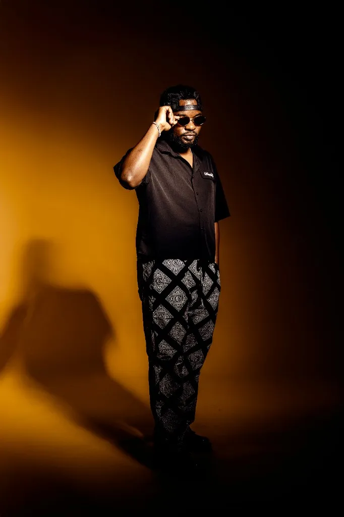 Ally Fresh adjusting sunglasses in patterned trousers against a mustard backdrop