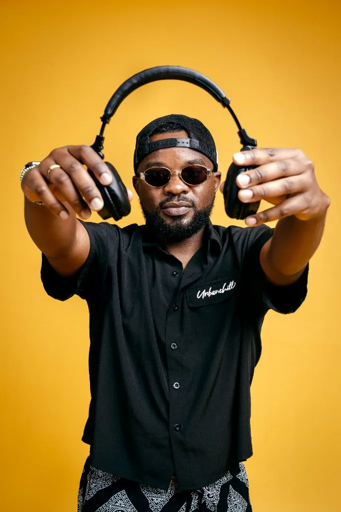 Ally Fresh holding headphones toward the camera against a mustard yellow backdrop