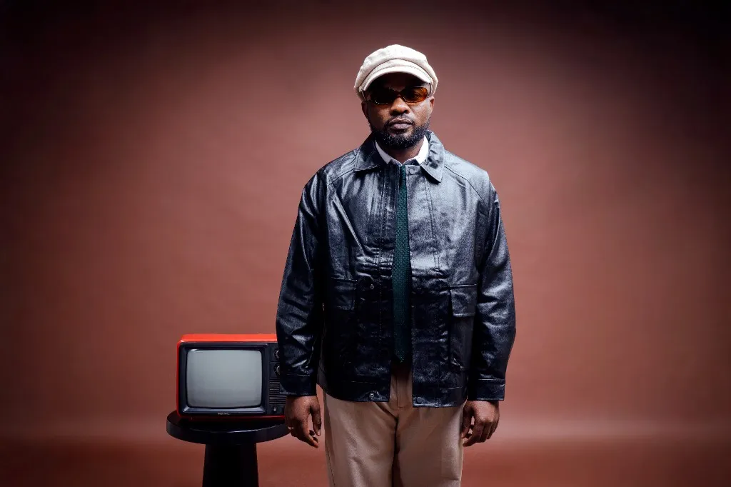 Ally Fresh in leather jacket, flat cap and sunglasses beside a vintage red TV
